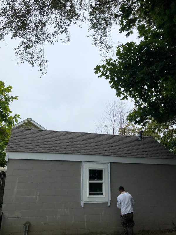 Asphalt roofing installed on garage with worker standing beside window